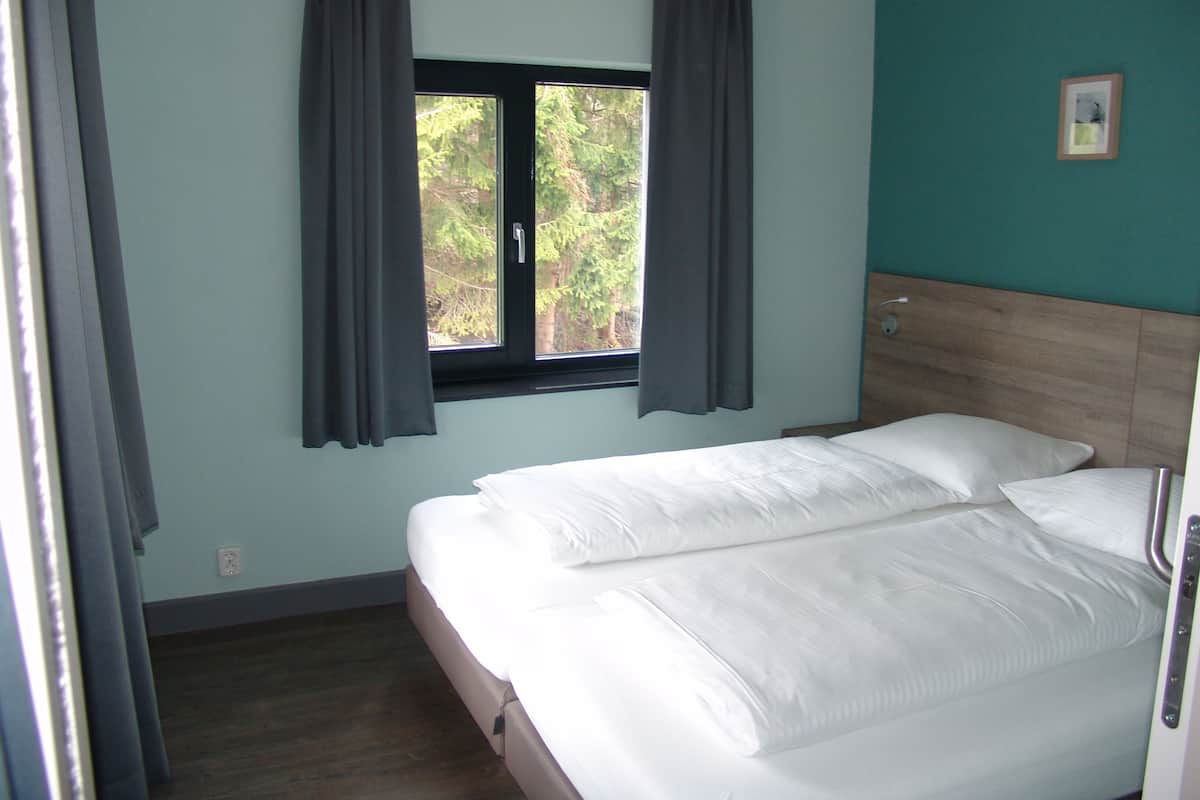Una camera da letto con un letto, una finestra con tende, una testiera e un piccolo quadro appeso al muro.