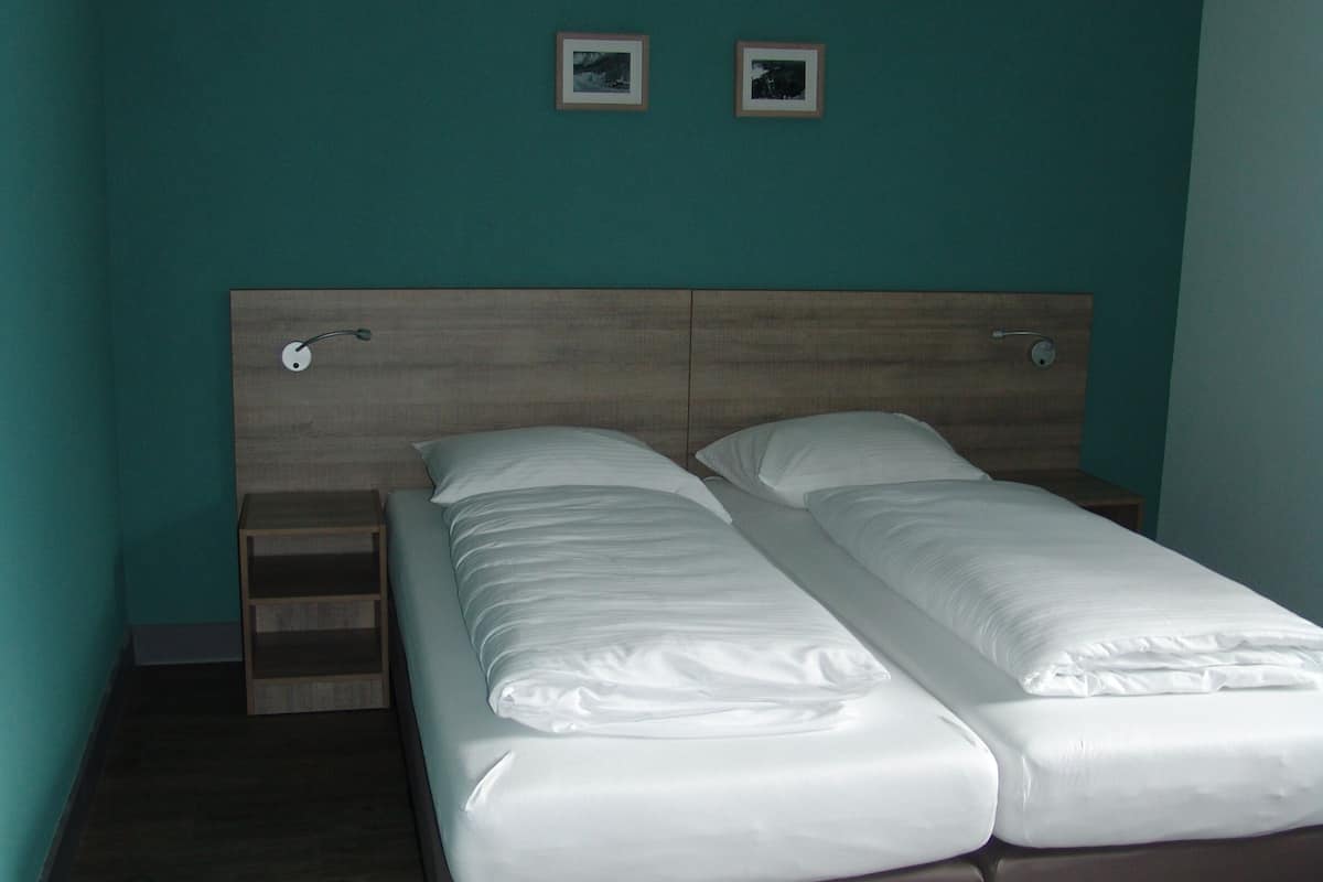 Una camera da letto con un poggiatesta in legno, due letti singoli, un comodino in legno e una mensola fissata al muro.