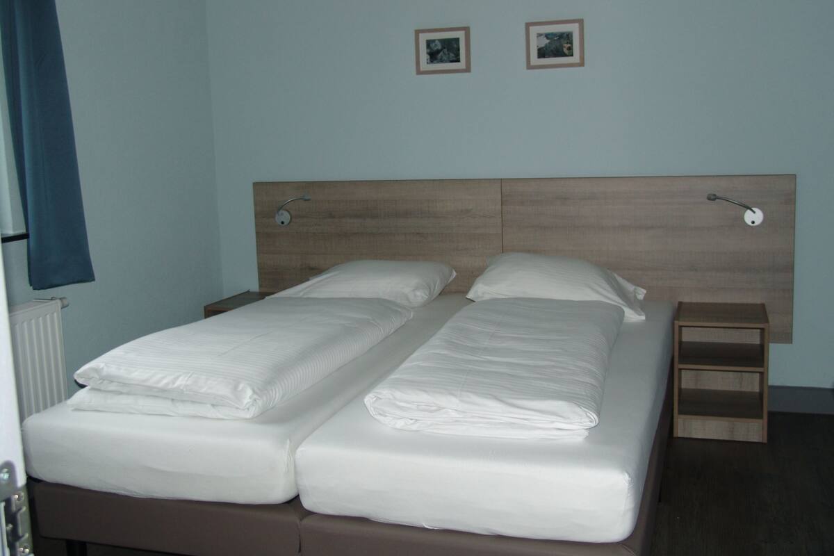 Un letto matrimoniale con testiera in legno, due comodini e due quadri appesi al muro.
