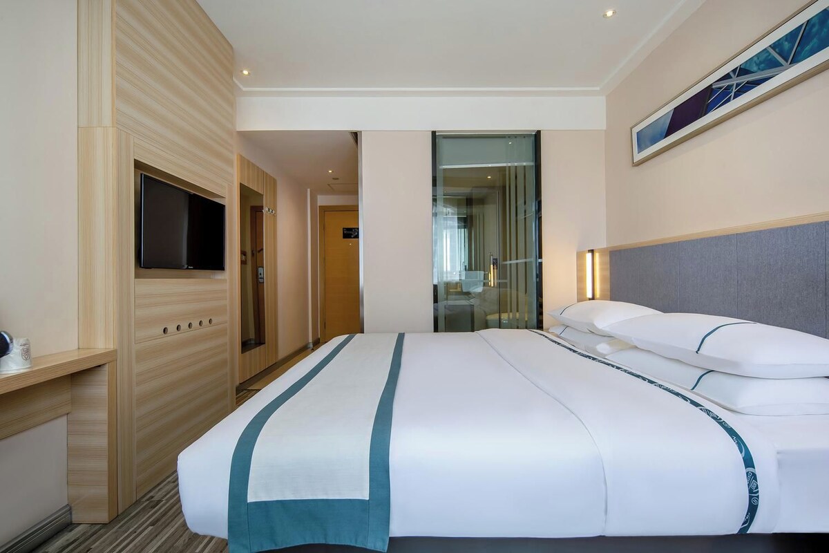 A hotel room with a bed, a television, and a bathroom visible through a glass door.