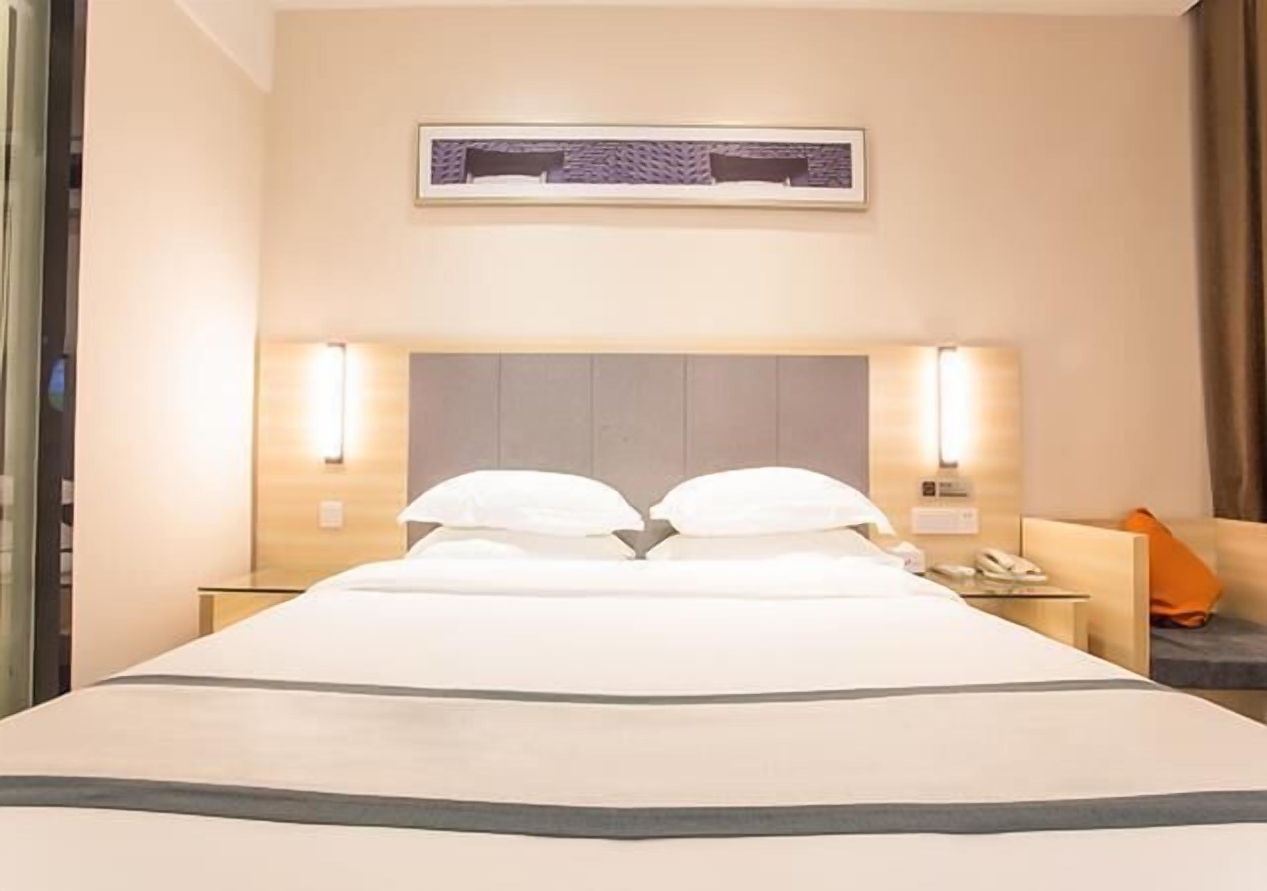 Una habitación de hotel con una cama, lámparas de noche, una mesita de noche y un cuadro en la pared.