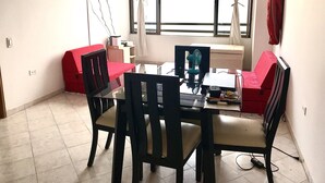 Zona pranzo con tavolo, sedie, televisione a parete e finestra con tende.