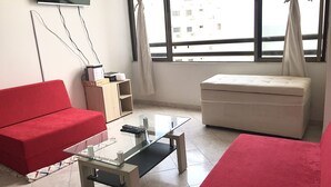 Un soggiorno con un divano rosso, un tavolino da caffè in vetro, un poggiapiedi beige e una TV a parete.