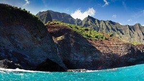 A coastal landscape with a prominent cliff, a waterfall, and a clear blue sea. - Amazing 1BR Condo in The Cliffs (Princeville)