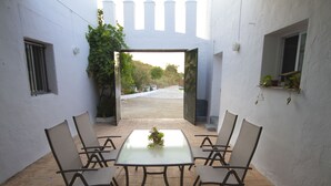 A patio with a table and chairs, a small window with plants, and a view of a garden.
