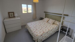 A bedroom with a bed, bedside table, dresser, window, and hanging lamp.