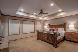 Une chambre à coucher avec un grand lit, un ventilateur de plafond, des spots encastrés, une tête de lit en bois et une table de chevet avec une lampe.
