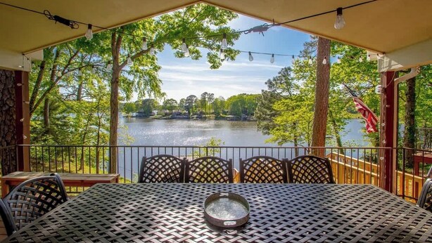 Un área de comedor al aire libre techada, con una mesa y sillas, con vista a un lago.