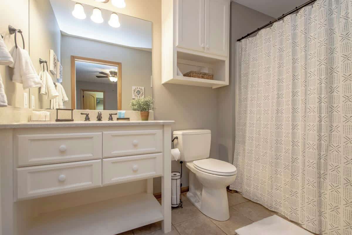 Ein Badezimmer mit weißem Waschtisch, Toilette, Duschvorhang und Deckenventilator.