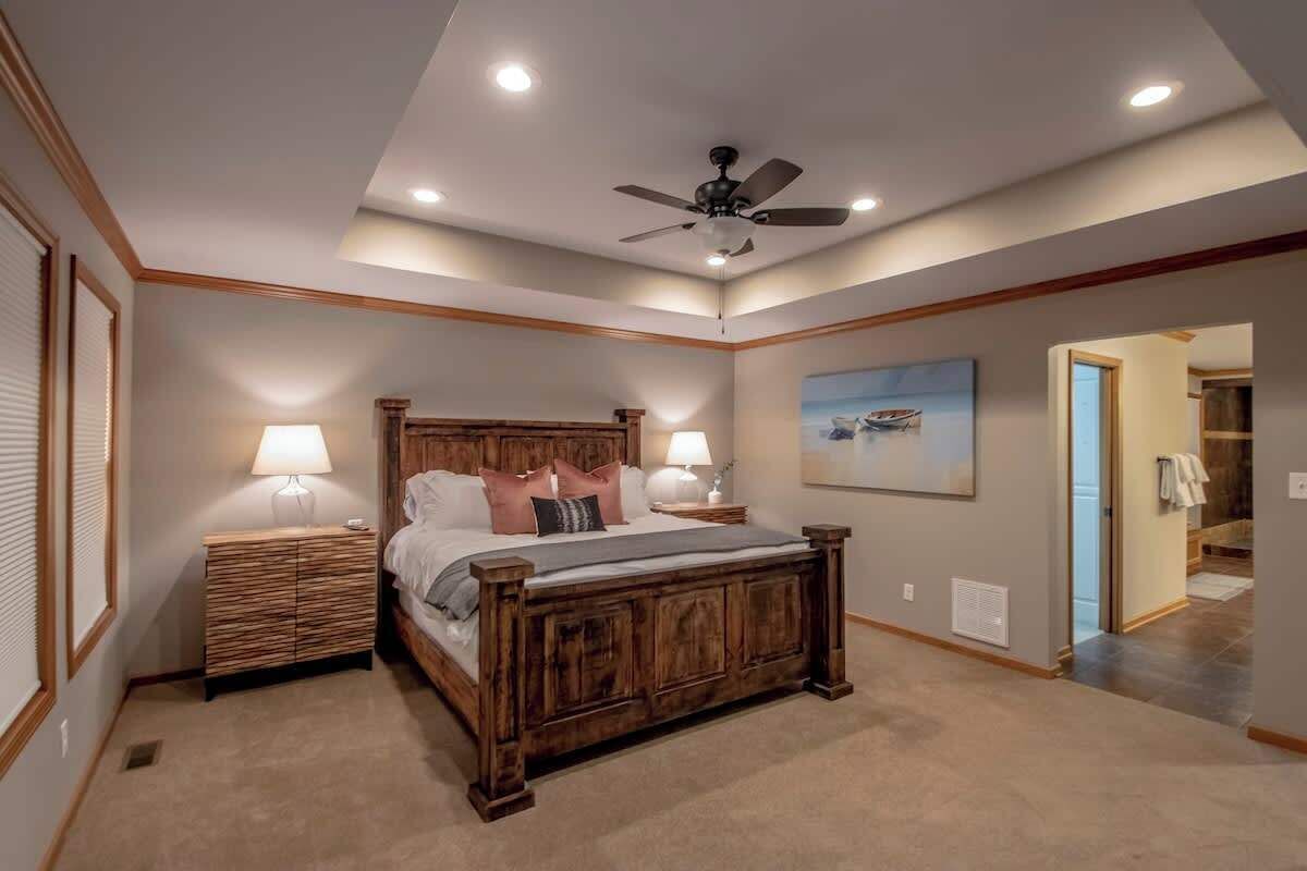 Une chambre à coucher avec un lit en bois, deux tables de chevet avec des lampes, un ventilateur de plafond, un éclairage encastré et un tableau au mur.