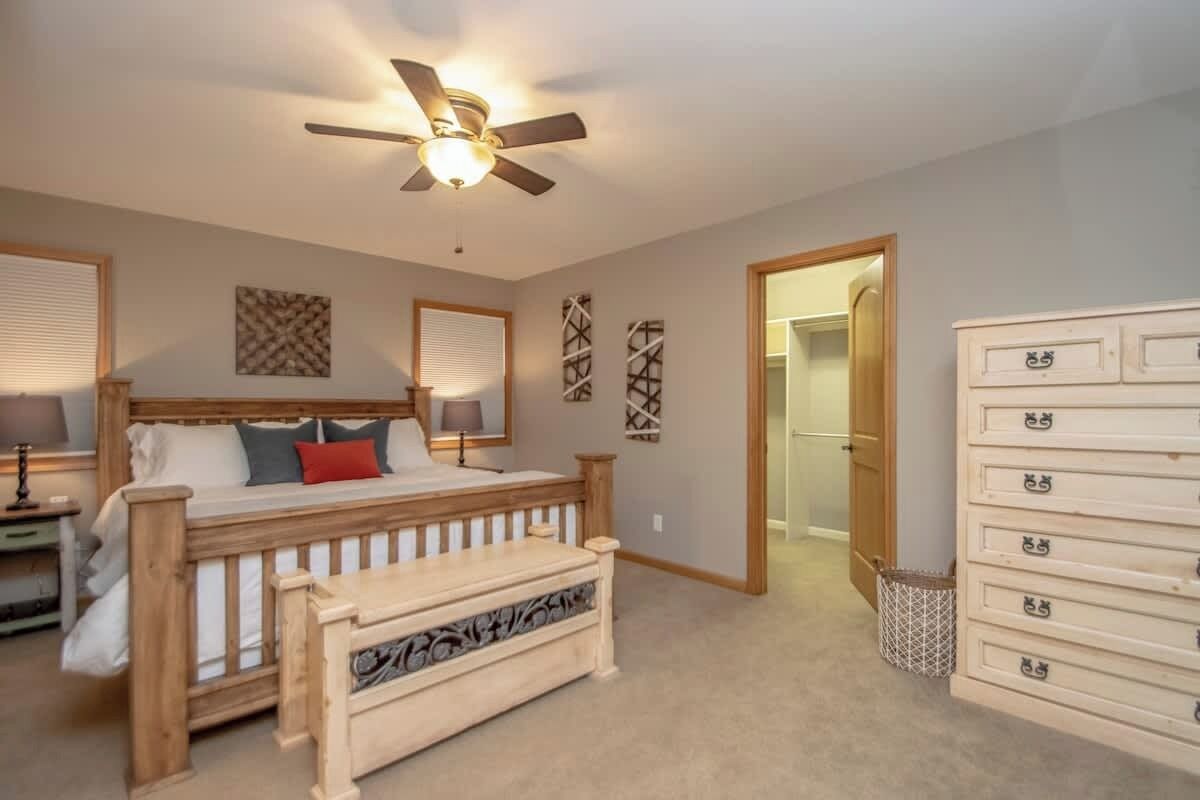 A bedroom with a bed, a ceiling fan, a dresser, and a door leading to another room.