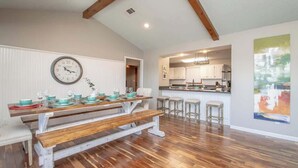 Una cocina amplia con piso de madera, una mesa de comedor preparada para cuatro personas y un reloj grande en la pared.
