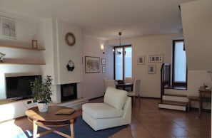 A living room with a TV, sofa, dining table, and chairs. There is a fireplace, a plant, and artwork on the walls. - Vacation apartment "THE CYPRESS" (Mori)