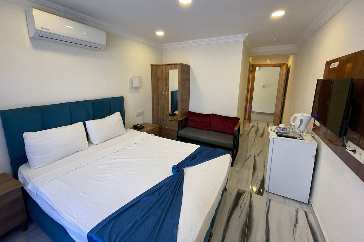 Ein Hotelzimmer mit Bett, Schreibtisch, Stuhl, Kleiderschrank, Spiegel und kleinem Kühlschrank.