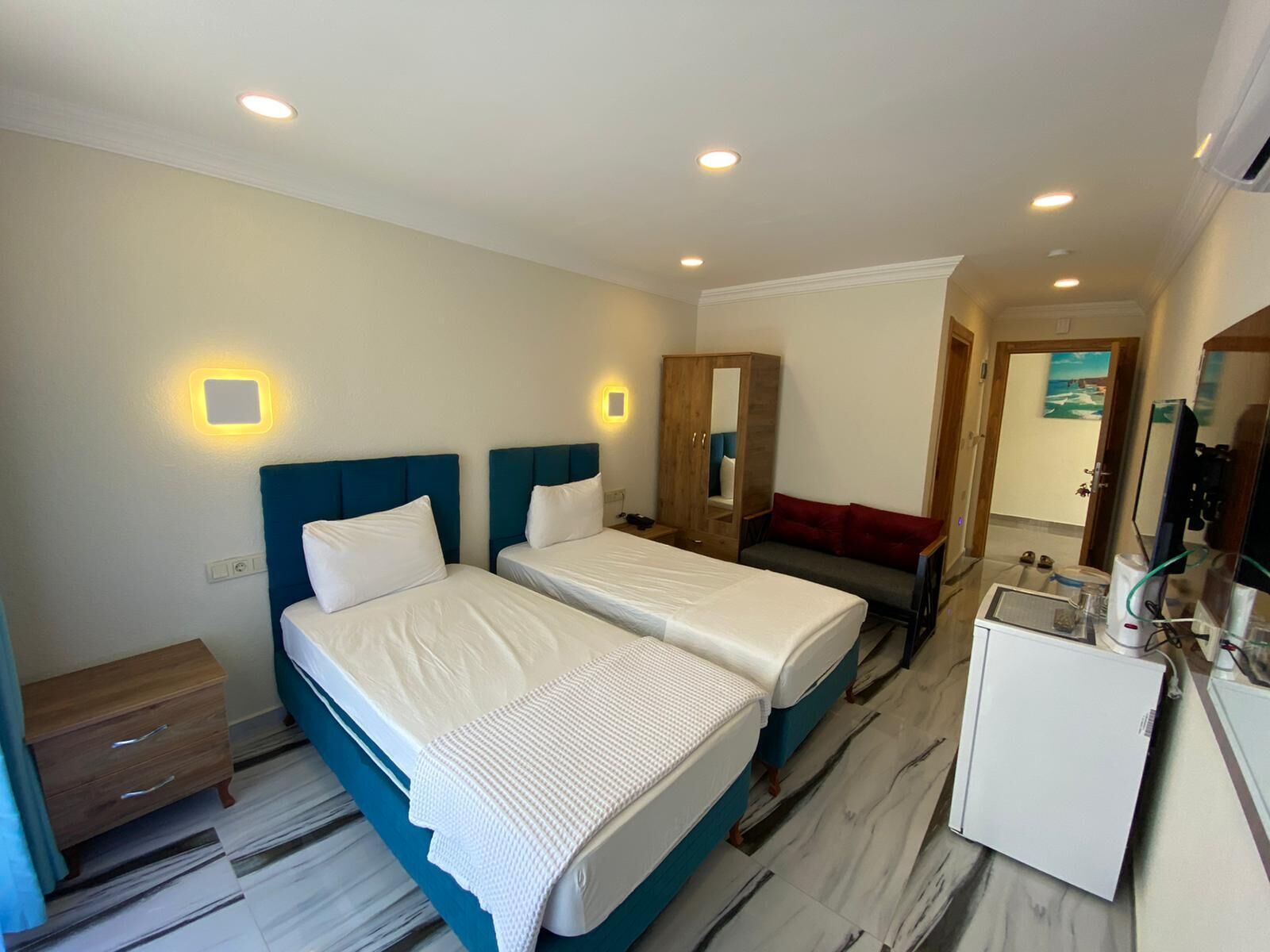 A hotel room with two beds, a wardrobe, a desk with a computer, and a mirror.