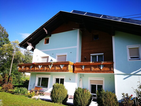 A two-story building with a balcony, solar panels, and a garden.