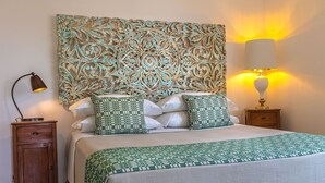 A neatly made bed with patterned pillows, a decorative headboard, a bedside lamp, and a small wooden nightstand. - Masseria Ferarelli - "Rizzeddrha" Room with Patio (Diso)