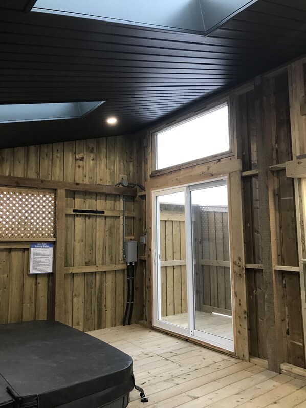 Una habitación con piso de madera, puerta corrediza de vidrio que da al exterior, ventilador de techo y un objeto negro en el suelo.