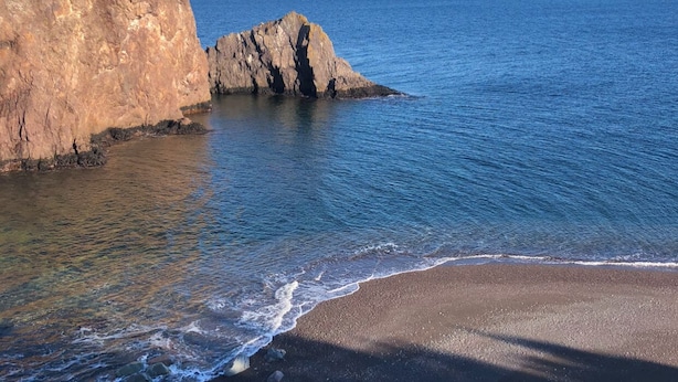 Paisatge costaner amb un penya-segat rocos i una platja de sorra.