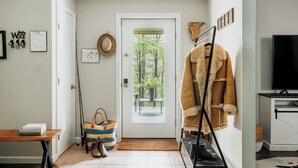 Ein Zimmer mit Holztisch, einer Tür mit Blick ins Grüne, einem Kleiderhaken mit einem Fellmantel und einem Fernseher auf einem Schrank.