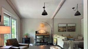 A cozy living room with a dining table, a sofa, and a coffee table. There are two pendant lights, a lamp, and a potted plant. - 50-Acre Riverfront Farm – Dog Friendly & Sleeps 6 (Milanville)