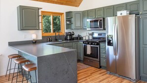 A modern kitchen with a large island, stainless steel appliances, and green cabinets. - Summer Cabin Retreat | Hot Tub, Firepit, Sleeps 12 (Alma)