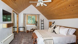 A bedroom with a sloped ceiling, a bed, a desk, and a window with curtains. - Summer Cabin Retreat | Hot Tub, Firepit, Sleeps 12 (Alma)