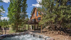 A wooden cabin with a hot tub, surrounded by trees and a clear sky. - Summer Cabin Retreat | Hot Tub, Firepit, Sleeps 12 (Alma)