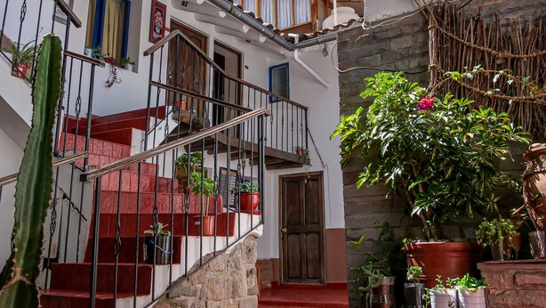 A narrow courtyard with a red-tiled floor, a staircase with potted plants, and a wooden door. - Hotel Guest House Wayra Cusco (Cusco)