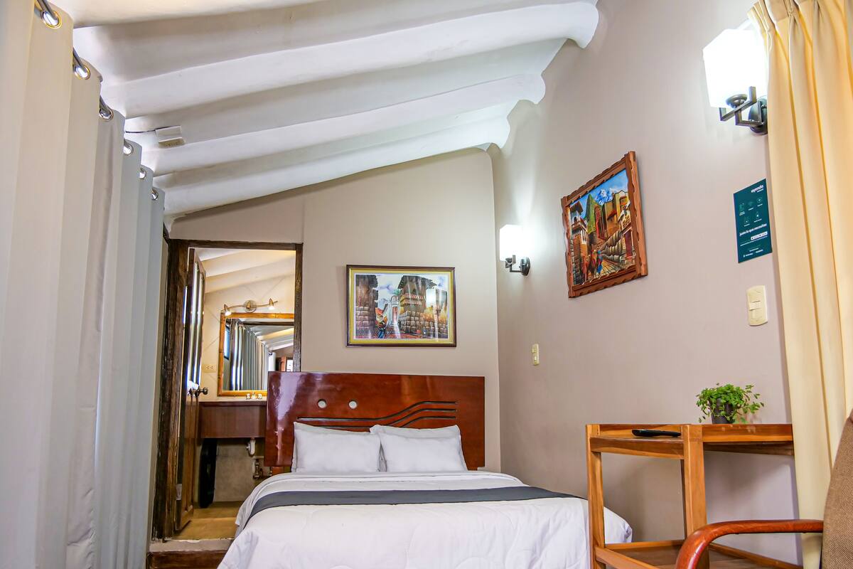 Ein Hotelzimmer mit einem Bett, einem Sessel, einem kleinen Tisch, einem Gemälde und einem Spiegel.