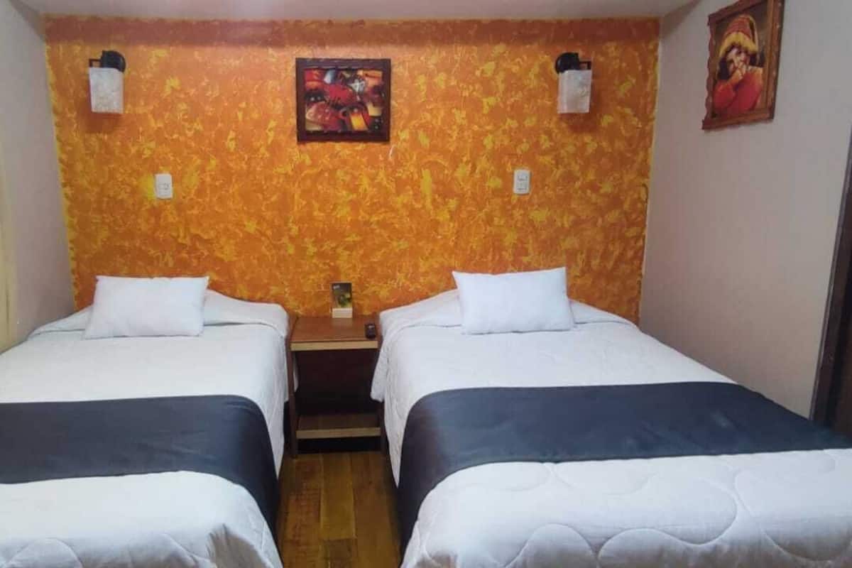 Ein Zimmer mit zwei Betten, Holzboden, einer Wand mit orangefarbenem Strukturmuster und einem kleinen Tisch mit Lampe.