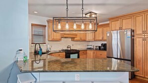 Une cuisine moderne avec des meubles en bois, un réfrigérateur en acier inoxydable, un plan de travail en granit et un luminaire suspendu.