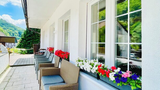 A covered outdoor seating area with wicker furniture and flower boxes on the windowsill. - AM BERG Hotel (Herzberg am Harz)