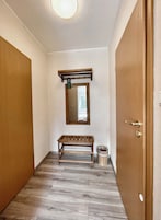 Un pasillo con suelo de madera, un banco, un cubo de basura y una puerta con cerradura.