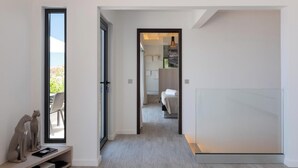 Un couloir d’hôtel moderne donnant sur l’extérieur, avec un lit et une salle de bain visibles à travers une porte ouverte.