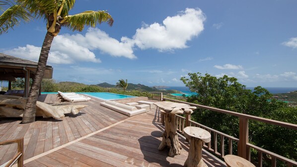 A wooden deck with lounge chairs and a pool, overlooking a scenic ocean view.