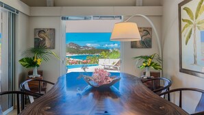 A dining area with a view of a coastal landscape, a table with a vase of flowers, and two potted plants. - Villa Sas (1/2 Rooms) (Saint Jean)