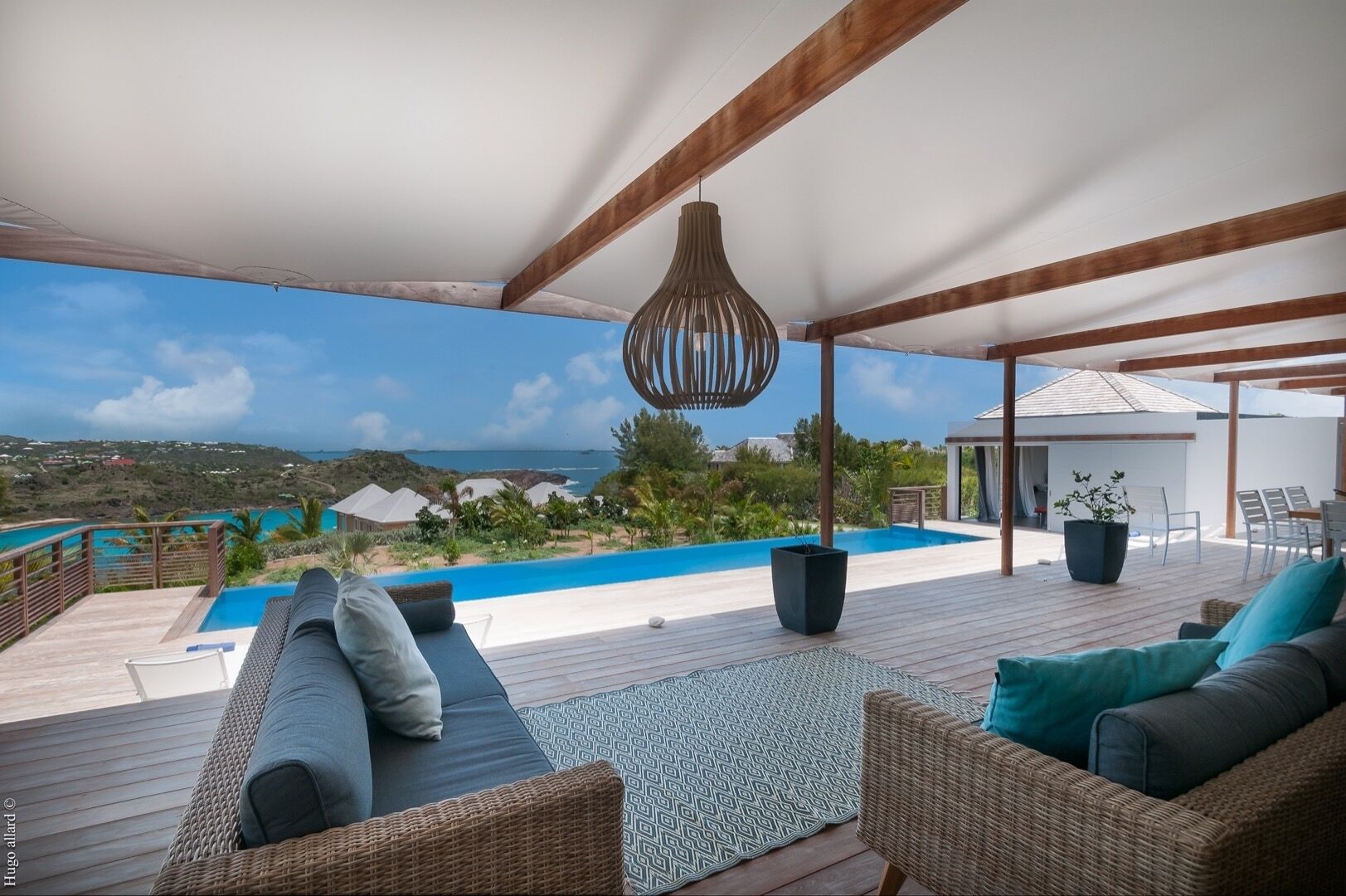 Un espacio al aire libre cubierto con piscina, muebles de mimbre y una lámpara colgante.