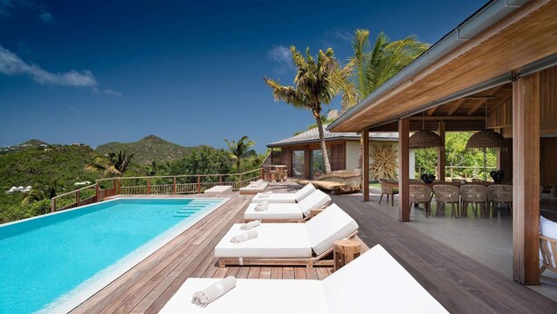 A poolside area with lounge chairs, a wooden deck, and a view of the surrounding landscape. - Beautiful Ixfalia Luxury villa (St Barts)