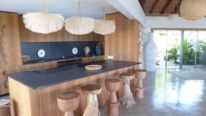 A modern kitchen with wooden cabinetry, a central island, and three hanging light fixtures. - Beautiful Ixfalia Luxury villa (St Barts)