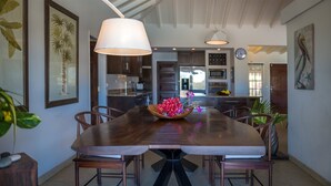 A dining area with a long wooden table, six chairs, a central floral arrangement, and pendant lighting. - Villa Sas Luxury villa (Saint Jean)
