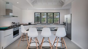 A modern kitchen with white cabinetry, a dining table with four chairs, a large window with blinds, and a ceiling fan. - Cairn (3/4 Rooms) Luxury villa (Petit Cul de Sac)