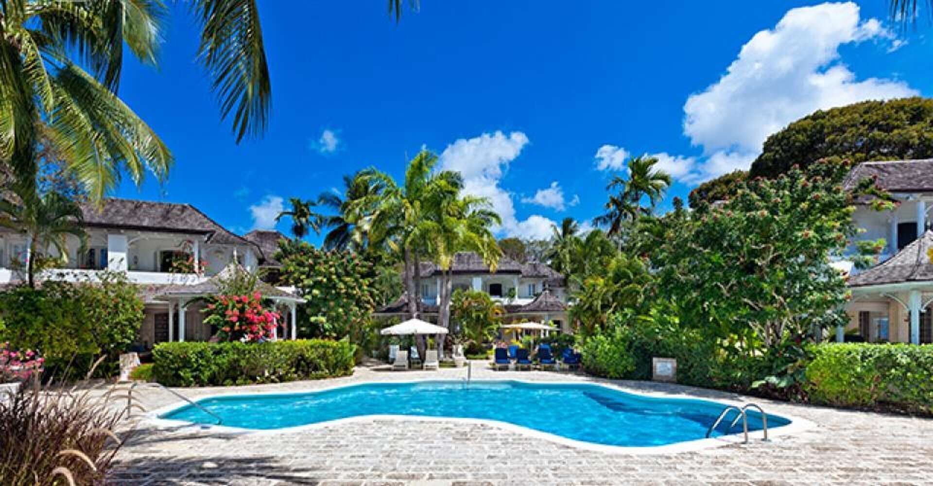 A resort with a swimming pool surrounded by palm trees and tropical plants.