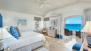 Ein geräumiges Schlafzimmer mit einem großen Bett, einem Schminktisch, einem Sessel und Meerblick.