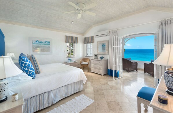 A spacious bedroom with a large bed, a vanity, a chair, and a view of the ocean.