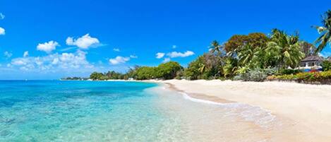 Una playa con agua turquesa cristalina, arena blanca y exuberante vegetación.