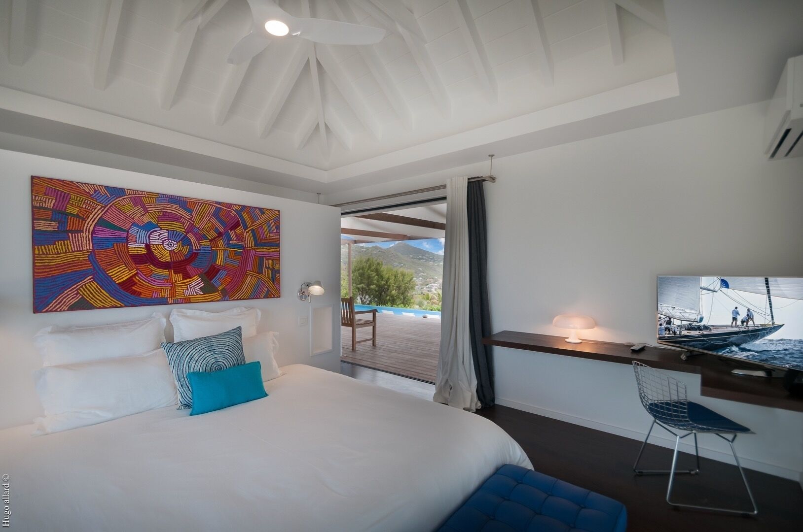 Ein modernes Schlafzimmer mit einem großen Bett, einem farbenfrohen abstrakten Gemälde, einem Fernseher und Blick ins Freie.