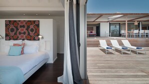 Une chambre moderne avec un grand lit, une vue sur la terrasse extérieure et un coin repas visible à travers une porte ouverte.