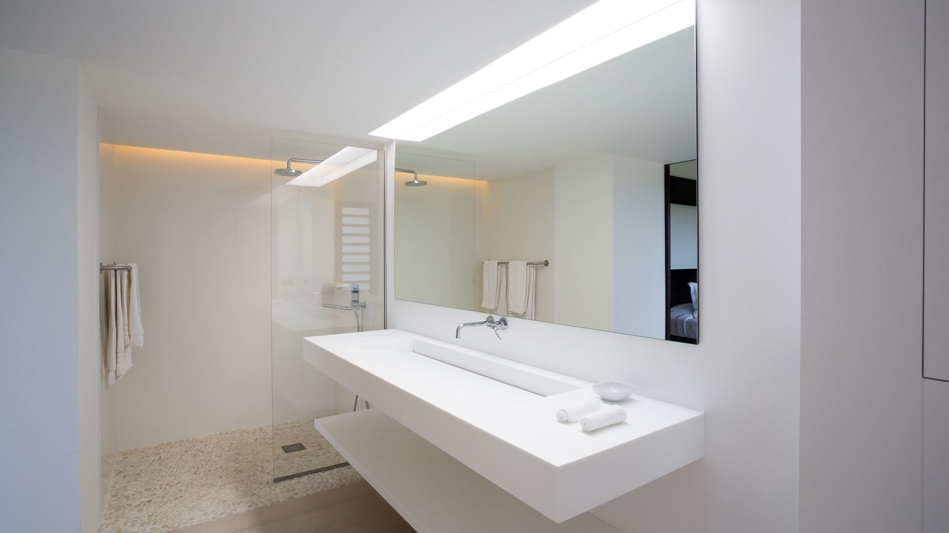 Une salle de bain moderne avec un grand miroir, un meuble-lavabo blanc et un espace douche.