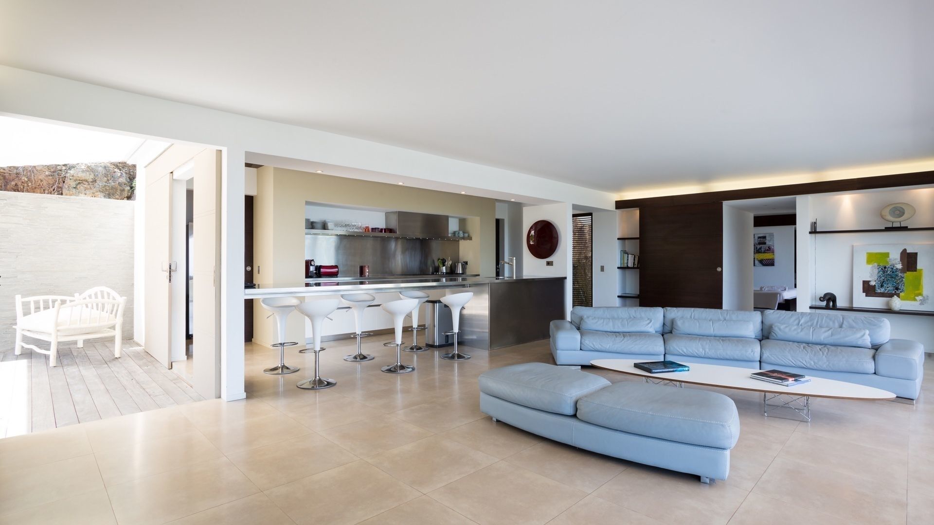 A modern living room with a light blue sofa, a coffee table, and a kitchen area with a bar and white bar stools.